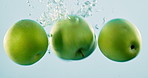 Apple, nutrition and natural fruit with water for vitamin c, fresh produce or hydration in studio on a blue background. Closeup of organic green food, juicy or sweet splash for healthy diet or fiber