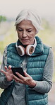 Senior woman, headphones and phone for fitness, retirement and cardio health outdoor while running. Elderly person, mobile and music app for streaming, exercise and podcast in nature as vertical