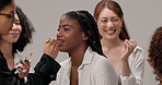 Beauty, product and women with makeup artist in studio for cosmetics, application or service. Happy, friends and group of people with beautician for glamour, glow or transformation by gray background