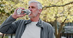 Runner, drinking water and senior man in park for health, wellness or hydration with fitness or nutrition. Tired, bottle or thirsty elderly person in outdoor training, workout or exercise rest break