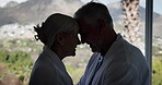 Happy, senior couple and holiday with hug by window for marriage, bonding or vacation on anniversary. Man, woman and affection with love in house for weekend getaway, romance or commitment connection