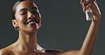 Face, woman and spray for makeup, mist and mockup for cosmetics on gray studio background. Female model, happy and smile for beauty, application and facial setting on skin for hydration and glow