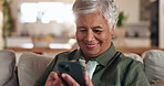 Senior woman, phone and smile on sofa, texting and reading with mobile app for contact in home. Person, smartphone and scroll with chat, notification and social network on lounge couch in retirement