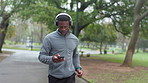 Running, phone and black man with headphones in park to listen to music, audio and radio for workout. Sports, nature and person with health app for marathon training, exercise and running outdoors