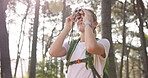 Travel, explore and woman with binoculars in nature for bird watching, vacation and outdoor adventure. Summer, journey and female person trekking in forest for backpacking, activity and observation