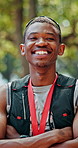 Medal, crossed arms and face of black man at race in nature with pride for fitness goal or achievement. Happy, win and portrait of African athlete with gold award for marathon with cardio exercise.