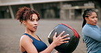 Outdoor, fitness and women in city with medicine ball, arm muscle and wellness on ground. Weight training, friends and athlete with workout, exercise and gear with balance, sport and downtown