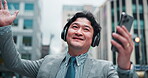 Japanese businessman, talking and video call in city with smartphone, mobile app and wave with contact. Urban, male realtor and hello with headphones for listening, networking or sightseeing in Tokyo