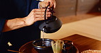 Person, tea ceremony and hands with teapot with matcha for Japanese tradition with culture, wellness and drink. Herb, ceramic kettle and cup for traditional detox, health and herbal custom at table