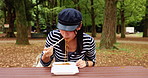 Woman, eating and park with food, noodles and picnic bench in Japanese forest with chopsticks and college student break. Outdoor, takeaway and calm in autumn and Japan on weekend with meal to relax