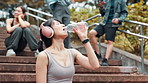 Woman, outdoor stairs and drinking water for fitness, running break and headphones for music. Female person, athlete relax and mineral liquid for thirst in Japan, sports and cardio rest in park