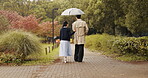 Umbrella, back and Japanese couple in park for love, partner and bonding together. Commitment, support and date with asian man and woman walking in nature path for care , honeymoon and vacation