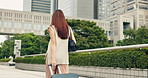 Woman, back and tourist walking with suitcase in city for travel, trip or immigration at indonesia. Female person, traveler or commute with mobile smartphone or luggage for destination in urban town 