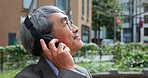 Mature man, headphones and thinking on business trip in city for music, travel and reading on sidewalk bench. Professional person, reflection and inspiration with sound, streaming and road in Japan