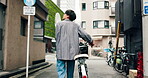 Man, walking and bicycle in city for travel, location and building with adventure, commute or trip. Asian person, back and bike in urban town for eco friendly transport, exercise or morning in Japan