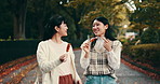 Happy, women and friends eating street food, walking and talk on commute to travel to Japan. Asian girls, together and smile with snack or dango outdoor at park for vacation, holiday or conversation