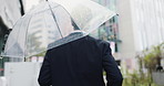 Rain, city road and Japanese man with umbrella and professional on morning commute in winter. Back, outdoor and cold weather on urban street with worker, travel and Tokyo trip in storm with journey