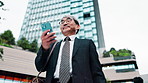 Mature businessman, smartphone and travel in city with texting, notification and low angle on commute to work. Person, phone and happy with mobile app, email and contact on urban sidewalk in Japan
