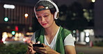 Man, headphones and phone at night in city, scroll website and streaming online for playlist. Male person, relax and outdoor music for peace in Japan, browse social media and internet for sound