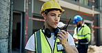Outdoor, man and speaking on radio at construction site for communication and connection for building project. Male person, employee and smile as engineer for inspection, supervision and architecture