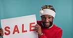 Christmas, face and man with sale sign poster for holiday, dancing and celebration on blue background. Portrait, excited and African person in studio for festive season discount, bargain and deal