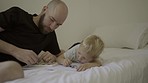 Father, child and drawing in a family home bedroom for creativity, art and learning. Man or dad and kid or son together on a bed to draw with crayons and paper for bonding and quality time in a house