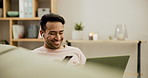 Asian man, headphones and laptop with dancing on sofa, happy and streaming podcast subscription in living room. Person, smile and smartphone for funny joke, relax wellness and freelancer in apartment