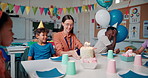 Children, teacher and cake for birthday party in classroom with friends and shy student at school. Kids, candles and happy people with food at celebration, social gathering and special event together