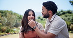 Couple, picnic and feeding at park, happy and bonding with memory, care and outdoor in summer. People, woman and man with food, snack and partner with helping hand for eating on date in Costa Rica