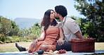Couple, kiss and picnic with smile at park, blanket and relax with memory, hug and outdoor on break in summer. People, woman and man with bonding on lawn, love and care with basket in Costa Rica