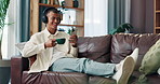 Phone, coffee and man with headphones on sofa in morning watching funny online video in home. Laughing, relax and male person in living room with cappuccino, cellphone and audio tech for streaming.
