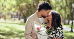 Couple, date and flowers in park with kiss, bonding and gift with partner commitment. People, happy and outdoor for relationship development, weekend relax or smile for love and anniversary picnic