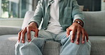 Hands, nervous and man on sofa with anxiety, stress or emotions in living room at home. Mental health, worry and male person rub leg for panic attack with phobia, overthinking or fear of trauma.