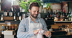 Waiter, man and cleaning glass in restaurant for hygiene, dirt removal and workflow inspection. Hospitality industry, happy barista and wipe glassware for disinfection, routine and bistro sanitation
