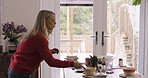 Woman, dancing and singing with music, cleaning and fun on living room tablet after breakfast in the morning. Mature female dance, audio and sing while collecting bowls after meal on table in home