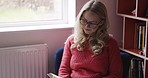 Book, knowledge and woman reading in a chair of her house, library or college. Education, learning and relax for a person with books for peace, information and studying in a living room of home