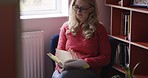 Book, smile and woman reading in a chair in her house, library or bookstore. Relax, calm and person with peace, information from books and knowledge from a story in a room or study in her home