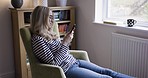 Relax, woman in living room and typing on smartphone with smile and coffee on armchair at window in home. Communication, technology and happy girl relaxing in apartment writing text or email on phone