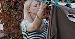 Laundry, clothes and hanging washing on clothesline by a mature woman at home in the garden. A lady doing chores, cleaning and drying wet, clean clothing on a line, outdoor in her backyard