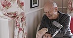 Laugh, talking and disability with a senior man sitting on a sofa in the living room of his home for recovery. Rehabilitation, physiotherapy and crutch with a mature male in his house for healing