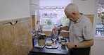 Senior man, morning and tea using kettle on kitchen counter during retirement and free time at home to relax. Elderly person in Uk house with tea bag or coffee drink for health and wellness