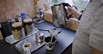 Senior man, hands and kettle for coffee on kitchen counter top in house or nursing home in morning routine. Retirement elderly, pensioner and old person with tea cup, hot water or drink in apartment