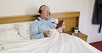 Senior man, bed and phone with music and headphones while relaxing in his retirement home. Retired elderly man, audio or streaming podcast while lying in his bedroom to relax and enjoy wifi