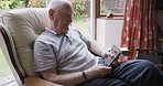Elderly man, smartphone and relax in armchair enoying retirement in living room home with peace, quiet and stress free. Senior person, cellphone and scroll social media online for news entertainment 