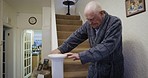 Senior man walking stairs in home with railing support for disability, osteoporosis and elderly help. Old man climbing down steps, staircase and independence in apartment, retirement and pensioner 