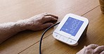 Elderly man, heart rate machine and blood pressure for monitoring, healthcare or BPM on table at home. Senior male checking heart monitor for medical cardiovascular health and wellness with high rate