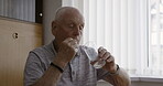 Senior man and wellness health pills at nursing home for self care, supplement and vitamin. Medicine, healthy and elderly retirement person drinking water with medication while thinking.

