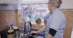 Nurse, caregiver and looking out kitchen window waiting for kettle to boil to make tea at nursing home at breakfast time. Healthcare, support and elderly woman working in senior care making coffee.