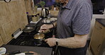 Old man cooking food at stove, kitchen and lunch meal at home. Senior male prepare dinner in pan for fresh, hot and healthy recipe in retirement, hungry pensioner and heating ingredients for eating