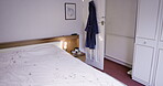 Bed, bedroom and morning in an empty home with a lamp next to an untidy blanket or bedding. Interior, background and sheet in a room during the day with a gown hanging on an open door inside